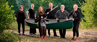 Sechs Musiker tragen ein Kanu