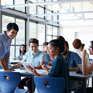 Eine Lehrerin spricht im Klassenraum lächelnd mit einer Gruppe von Schülern.