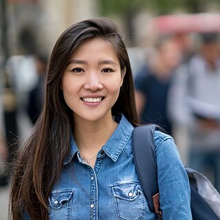 Porträt einer jungen Frau, Close-Up. Der Hintergrund ist unscharf, eine Personengruppe unterhält sich. Die Frau lächelt in die Kamera.