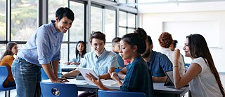 Eine Lehrerin spricht im Klassenraum lächelnd mit einer Gruppe von Schülern.