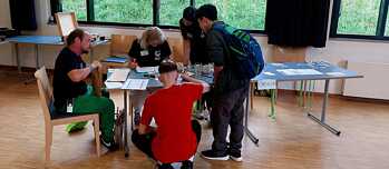 Fünf Personen sind um einen Tisch versammelt und blicken konzentriert auf Unterlagen.