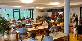 Eine große, helle Kantine, modern eingerichtet. Jugendliche sitzen an den Tischen und genießen ihre Speisen.