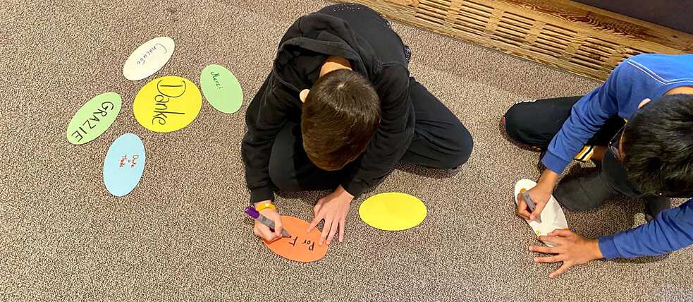 Jugendliche sitzen auf dem Fußboden und schreiben Begriffe auf bunte Karten.