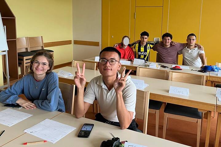 Jugendliche sitzen in einem Klassenzimmer an Tischen. Vor ihnen liegen Arbeitsblätter und Schreibgeräte.