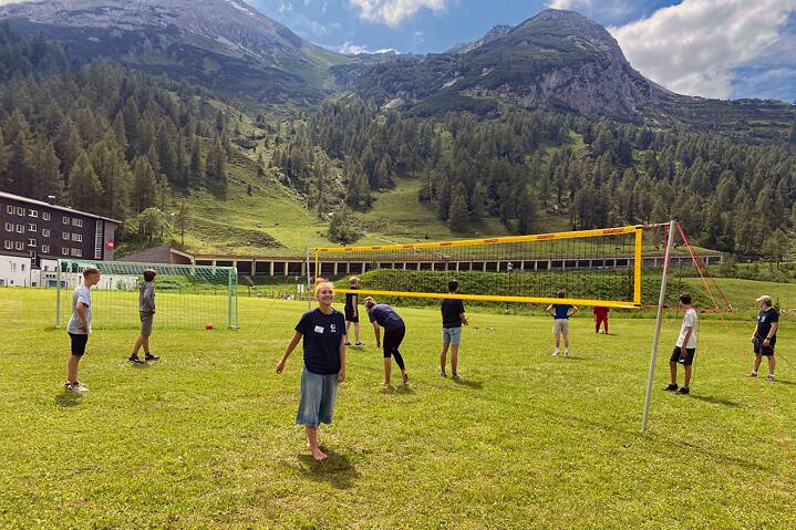Jugendliche spielen Volleyball auf einer Wiese. Im Hintergrund sind die Alpen zu sehen.