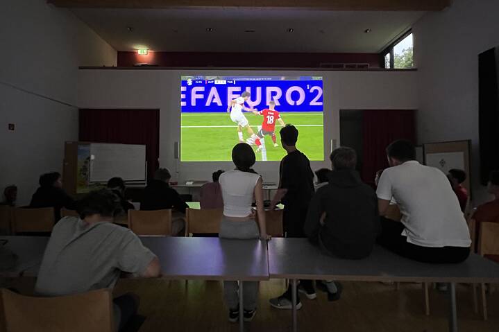  Jugendliche in einem dunklen Raum sehen ein Fußballspiel gespannt zu.