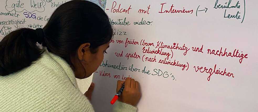 Eine Jugendliche schreibt auf ein großes, weißes Blatt einer Flipchart.