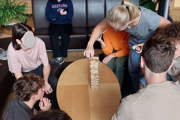 Jugendliche stapeln Jenga Spielklötze aus hellem Holz auf einem runden Tisch.