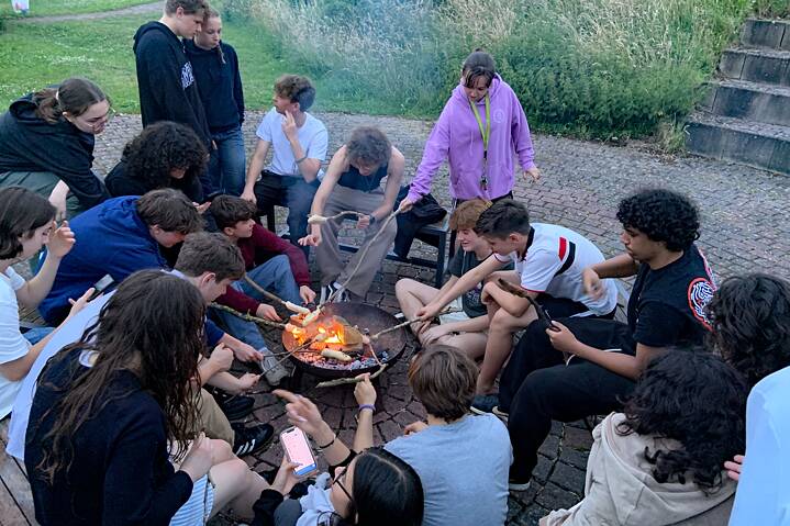 Jugendliche sitzen um eine Feuerschale und bakcen „Stockbrot“.
