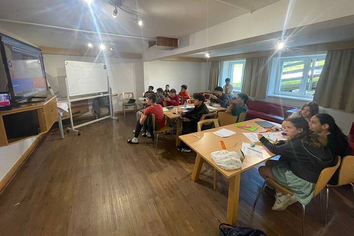 Jugendliche in einem Klassenraum arbeiten konzentriert. Vor ihnen flimmert ein großer Bildschirm.