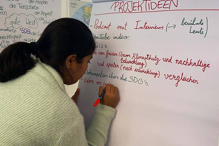Eine Jugendliche schreibt auf ein großes, weißes Blatt einer Flipchart.