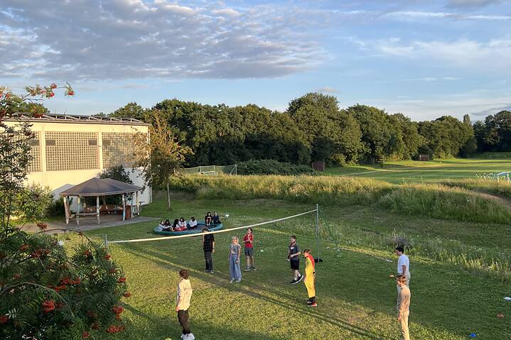 Jugendliche spielen Volleyball auf einer Wiese in der Abendsonne.