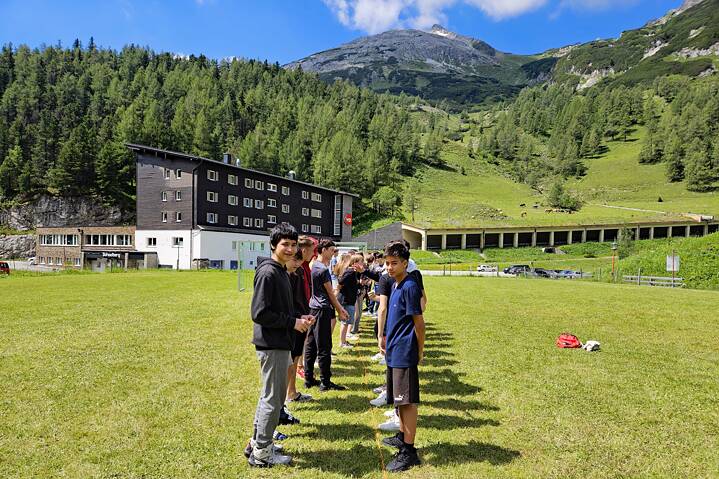 Jugendliche stehen in einer Reihe auf einer Wiese, im Hintergrund die Alpen.