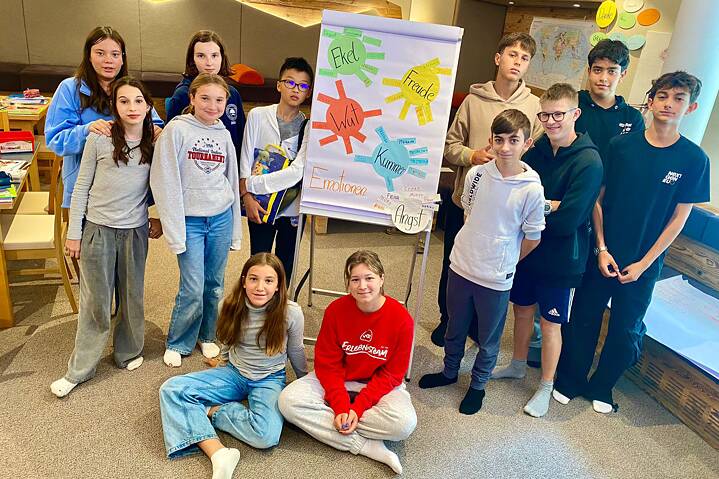 Eine Gruppe Jugendlicher lächtelt in die Kamera, zwischen ihnen steht eine Flipchart mit bunten Zeichnungen.