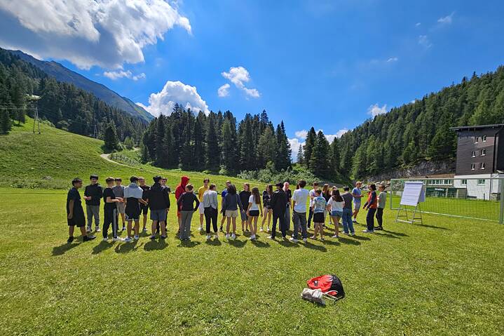 Jugendliche stehen in einer Reihe auf einer Wiese, im Hintergrund die Alpen.