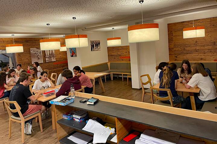 Jugendliche sitzen in Gruppen an Tischen in einem großen Raum und spielen.