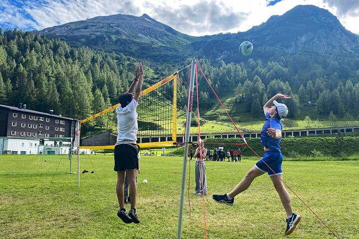 Jugendliche spielen Volleyball auf einer Wiese in den Bergen.