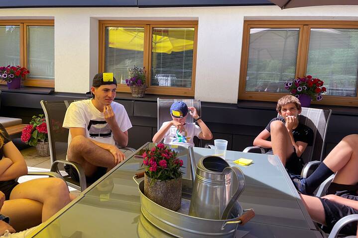 Jugendliche sitzt an einem Tisch unter Sonnenschirmen. An der Strine eines der Jugendlicher klebt ein Post-it.