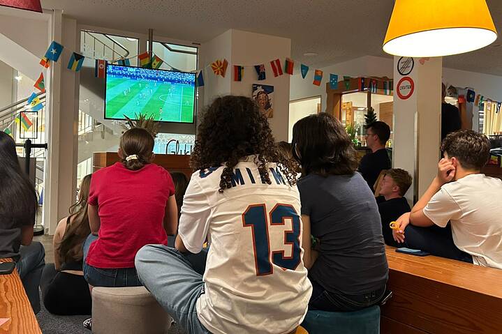 Eine Gruppe Jugendlicher blickt gespannt auf einen großen Fernsehbildschirm.