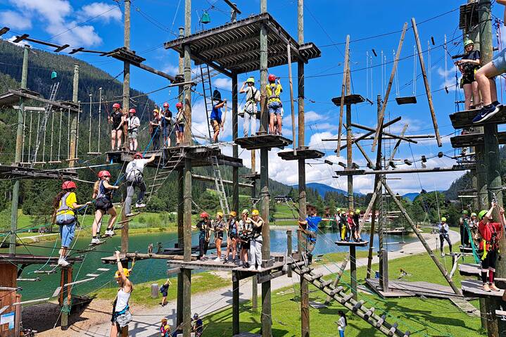 Jugendliche mit Sicherheitsausrüstung klettern in einem Hochseilgarten.