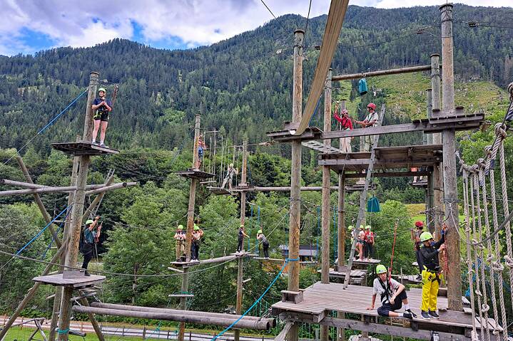 Jugendliche mit Sicherheitsausrüstung klettern in einem Hochseilgarten.