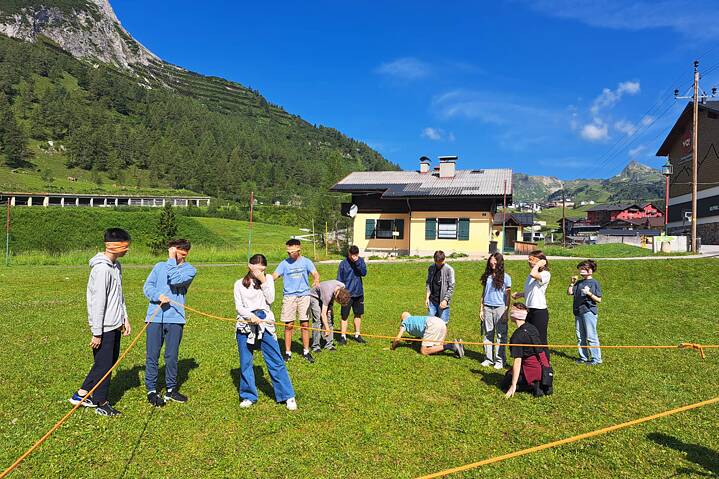 Jugendliche auf einer Wiese, um sie herum ist ein Seit gespannt, sie haben die Augen verbunden.