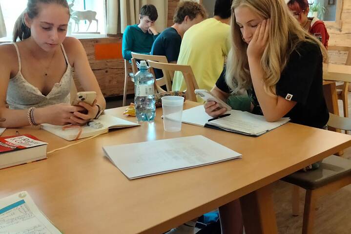Jugendliche sitzen an einem Tisch, sie halten Smartphones in der Hand und wirken konzentriert.