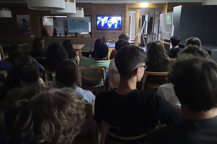 Jugendliche in einem Raum dunklen Raum. Auf einem Flachbildschirm läuft ein Film.