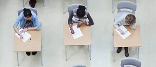 Blick von oben auf Schüler*innen an Einzeltischen, die gerade eine Prüfung schreiben.