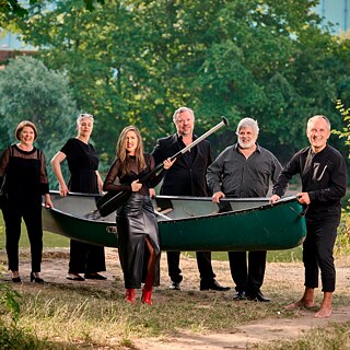 Sechs Musiker tragen ein Kanu 