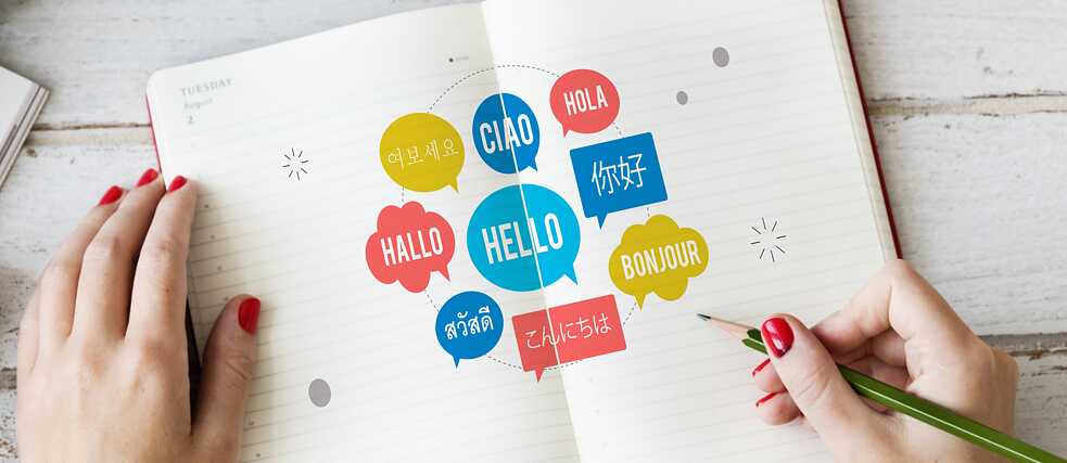 In einem Notizbuch stehen bunte Sprechblasen mit „Hallo“ in verschiedenen Sprachen.