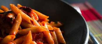 Penne mit Tomatensauce angerichtet auf einem dunklen Teller.