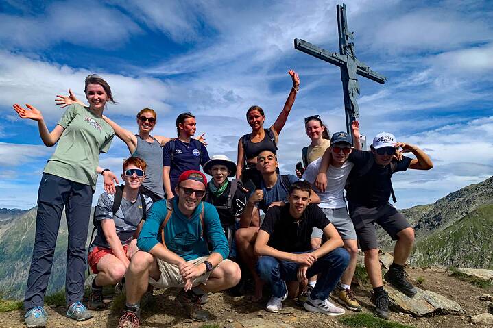 Eine kleine Gruppe posiert für ein Foto, hinter ihnen ein Gipflekreuz.