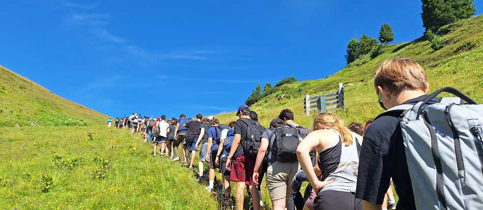 Jugendliche mit Rucksäcken auf einem Pfad in den Alpen