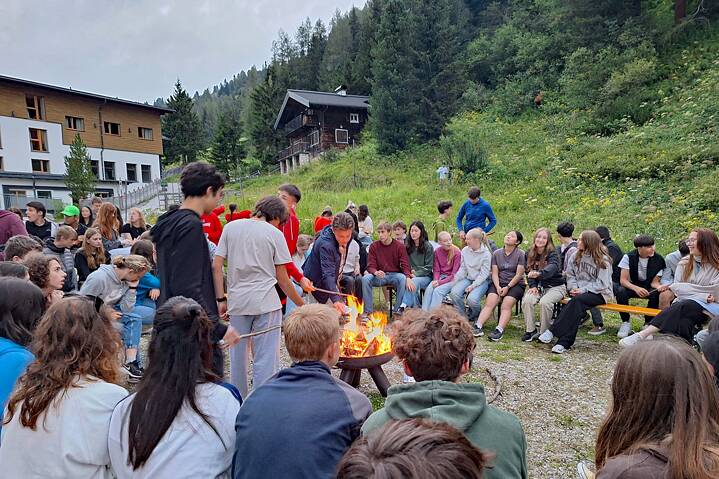 Jugendliche sitzen und stehen um ein Feuer und grillen Stockbrot.