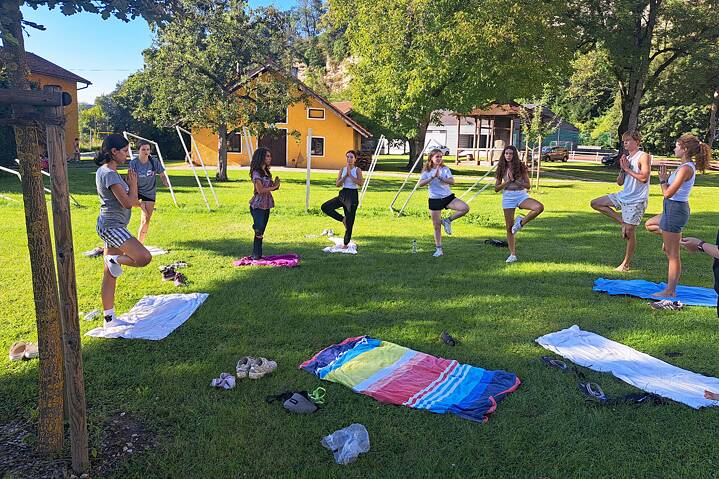 Jugendliche beim Yoga unter schattenspendenden Bäumen auf einer Wiese