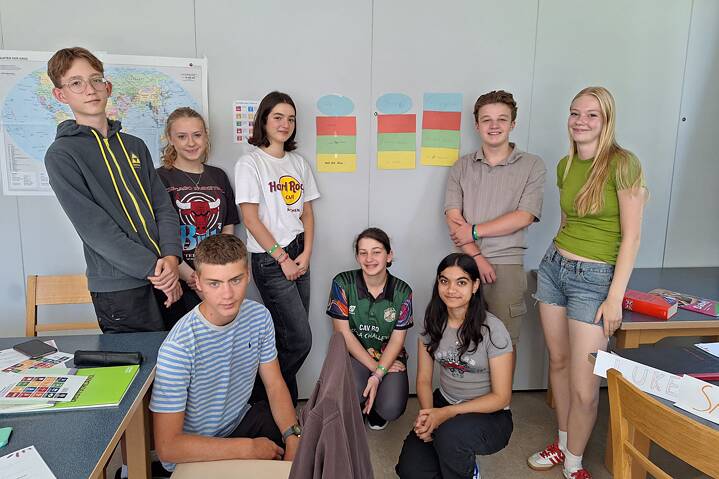 Eine kleine Gruppe Jugendlicher steht für ein Foto in einem Klassenraum.