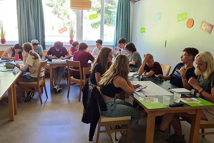 Eine kleine Gruppe Jugendlicher arbeitet konzentriert an Tischen in einem Klassenraum.