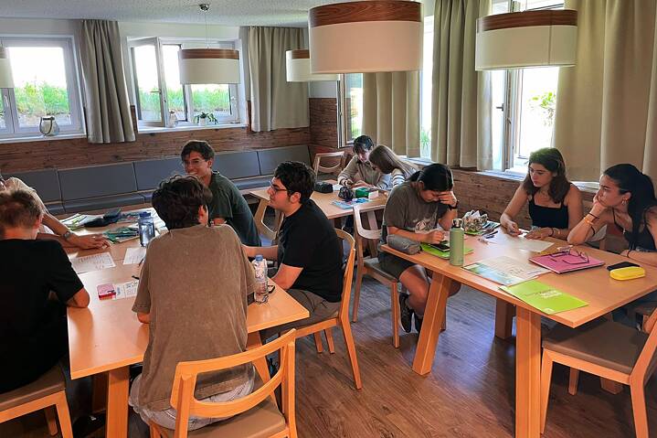 Eine kleine Gruppe Jugendlicher arbeitet konzentriert an Tischen in einem Klassenraum.