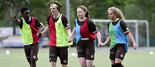 Four young people in football kit run across a football pitch, holding hands.