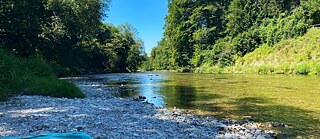 Auf einem steinigen Flussufer liegt ein Handtuch.