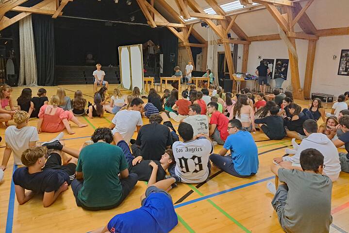 Jugendliche sitzen auf dem Parkettboden unter einem Holzgewölbe.