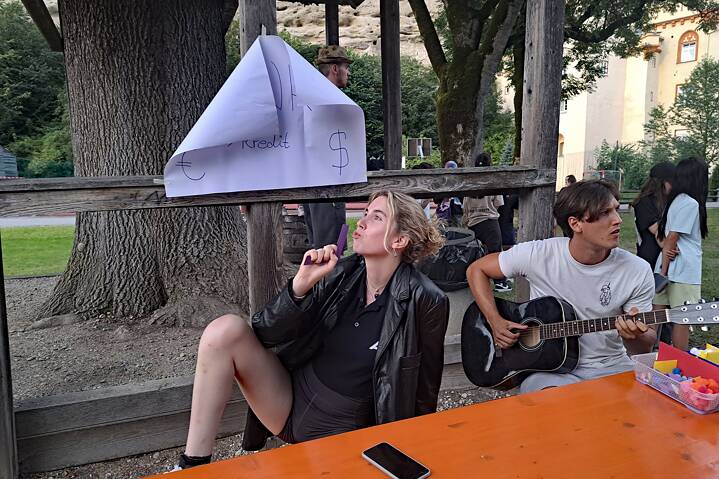 Junge Erwachsene an einem Biertisch, der eine spielt Gitarre.