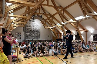 Jugendliche sitzen auf dem Boden, andere sind verkleidet und geben Anweisungen.