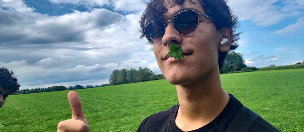 Jugendlicher mit Sonnenbrille auf der Nase und Kleeblatt im Mund