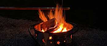 In einer Schale lodert ein Feuer, dahinter steht eine Bierbank.