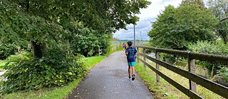 Kinder laufen auf einem Weg zwischen einem Wald und einer Wiese.