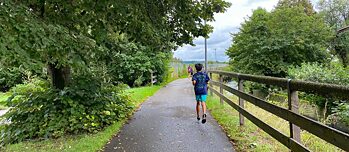 Kinder laufen auf einem Weg zwischen einem Wald und einer Wiese.