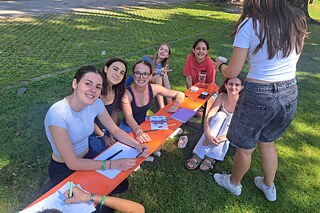 Jugendliche sitzen an einem Biertisch auf einer Wiese und lächeln in die Kamera.