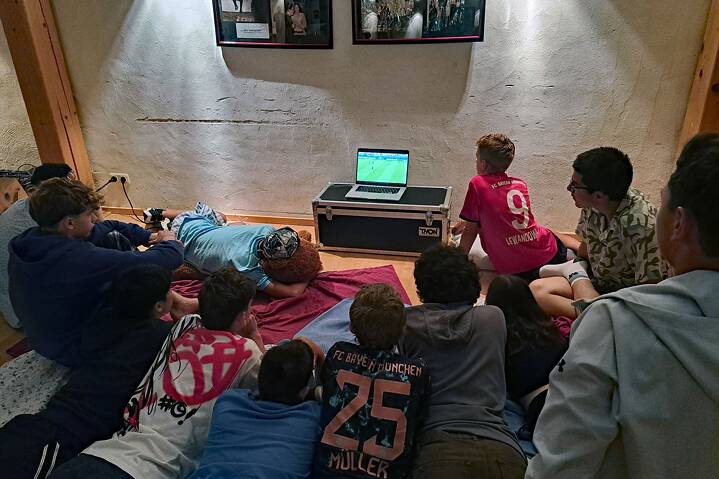 Kinder liegen auf dem Bauch und sehen ein Fußballspiel auf einem Laptop.